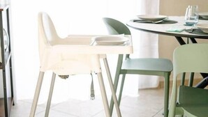Un comedor con una trona, una mesa dispuesta con platos y cubiertos, y un televisor de pantalla plana montado en la pared.