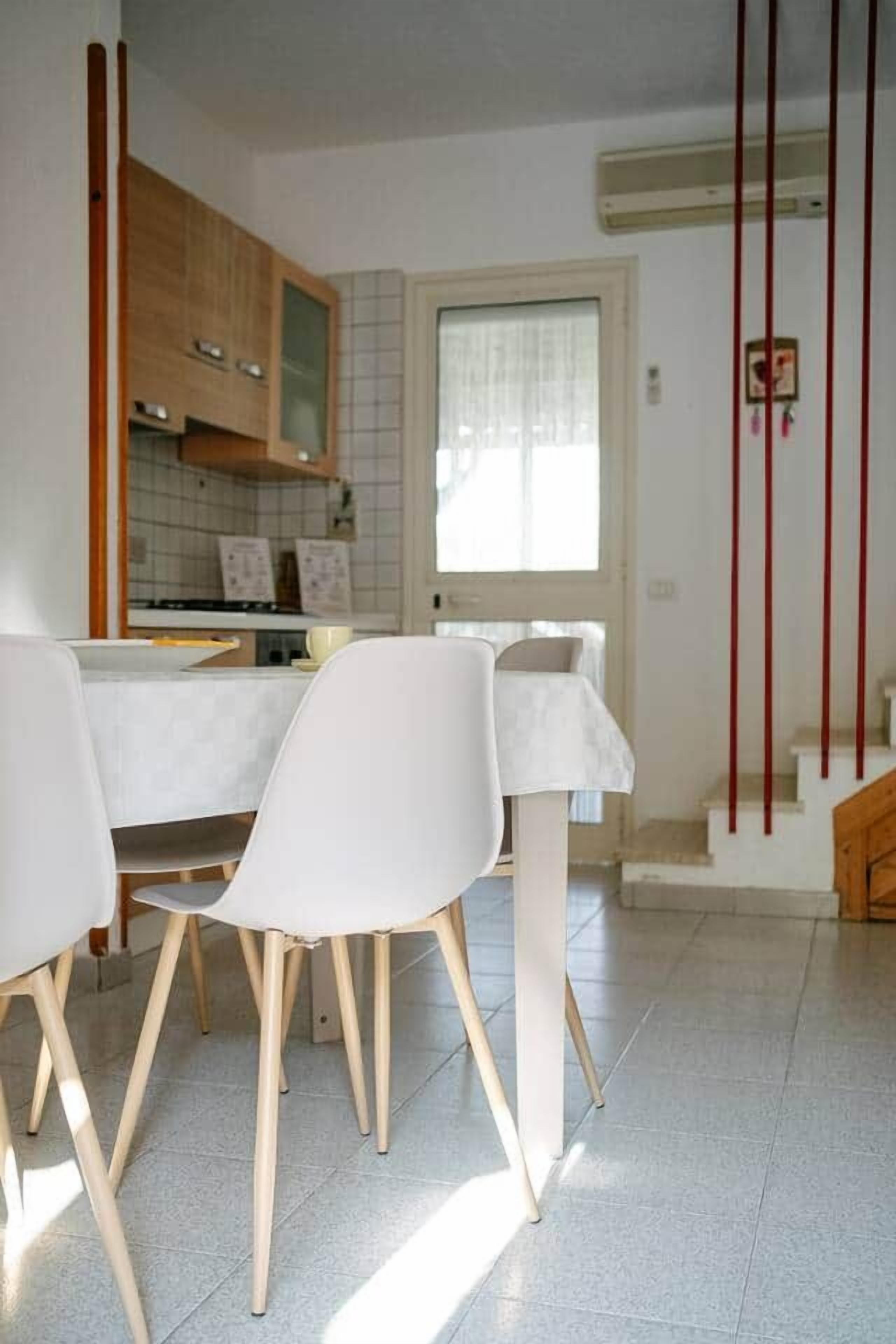 Un espace repas avec une table et des chaises, une cuisine à l’arrière-plan et un escalier menant à l’étage supérieur.