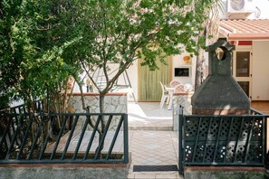 Une cour intérieure avec un mur en pierre, un portail en métal et un espace repas comprenant des chaises blanches et une table.