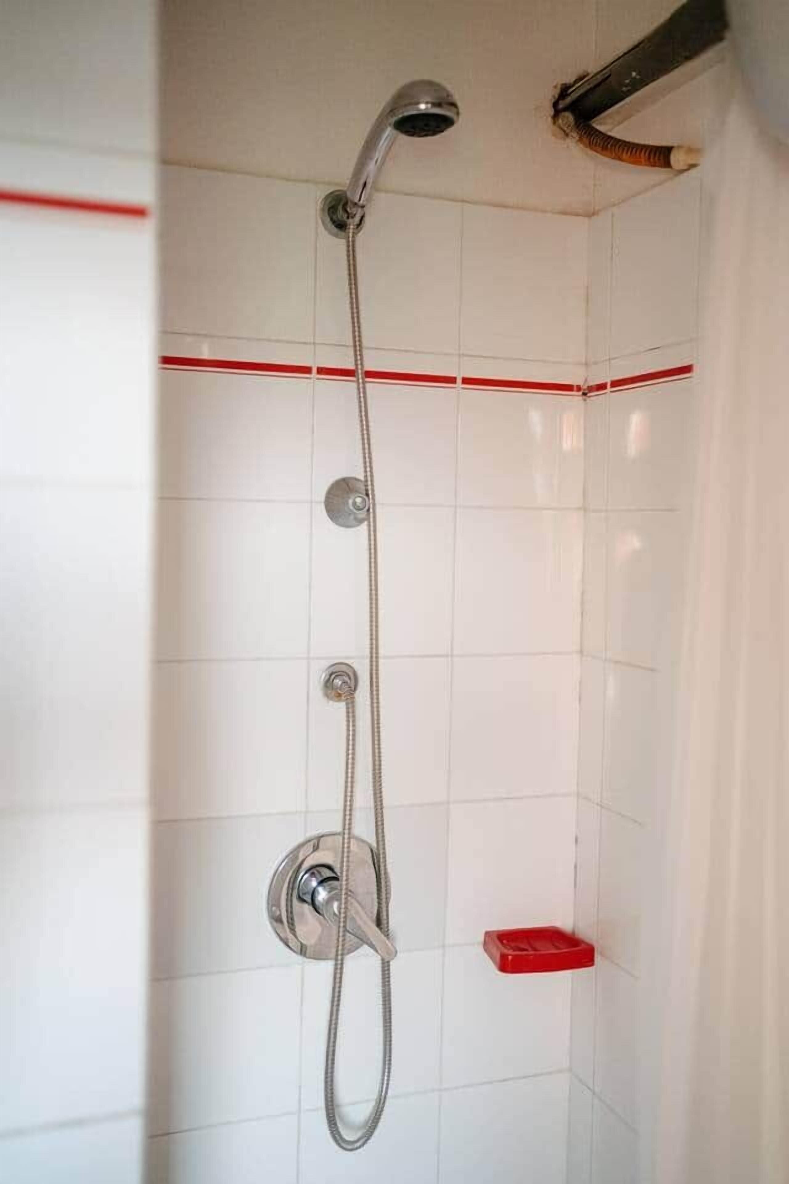 Une douche équipée d’un pommeau de douche à main, d’un robinet mural et d’un porte-savon rouge.
