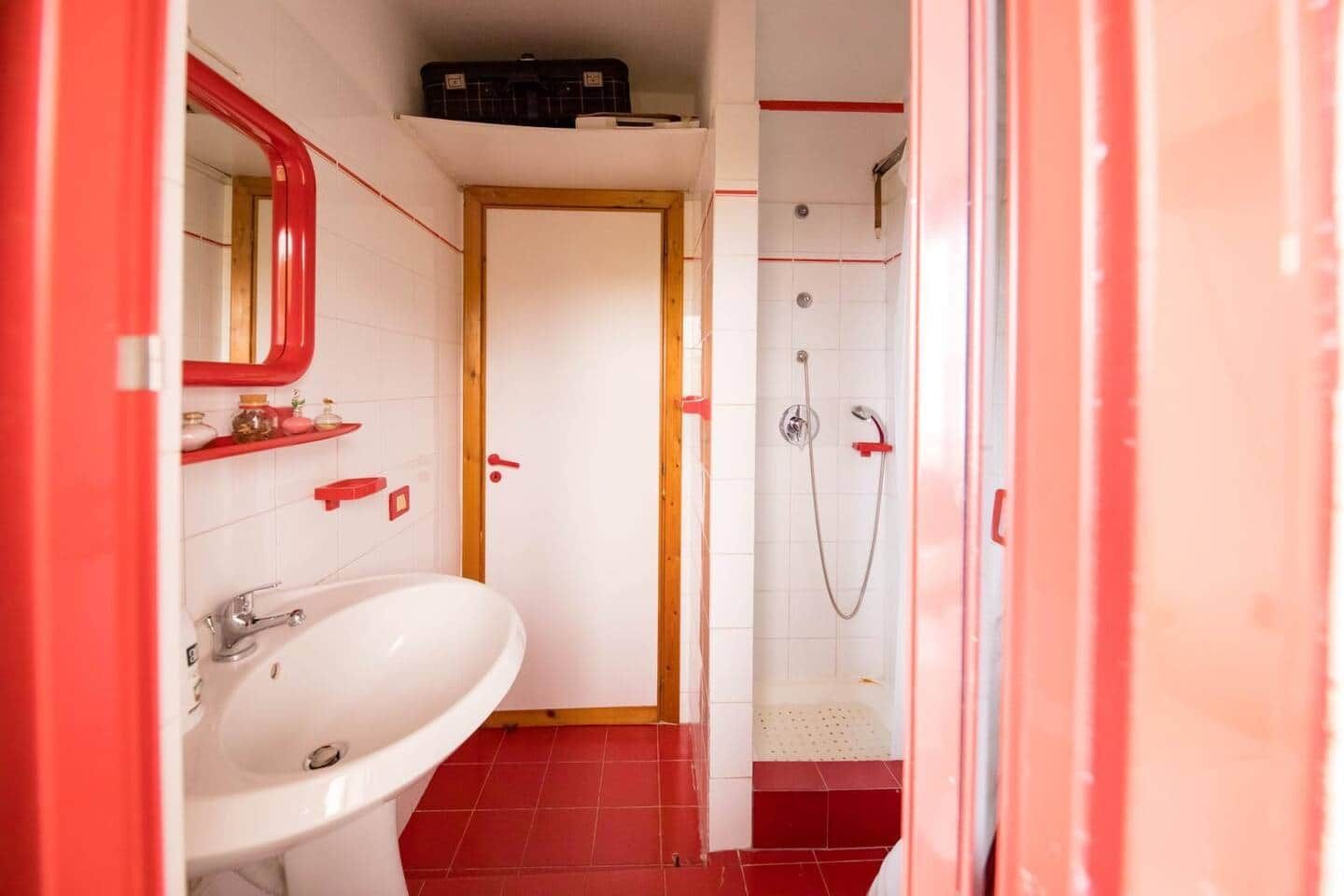 Ein Badezimmer mit einem weißen Waschbecken, roten Fliesen und einer roten Dusche.