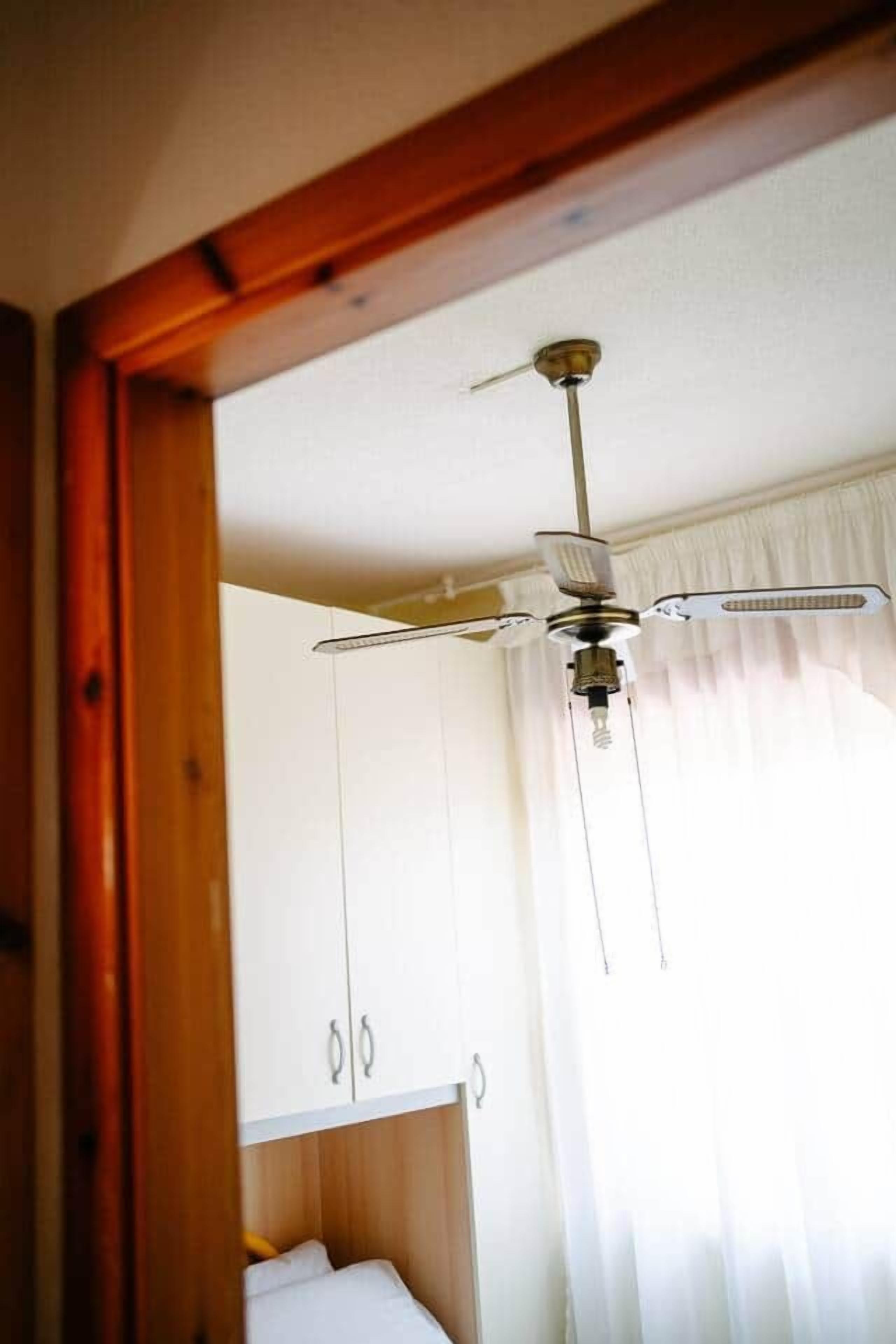 A room with a ceiling fan, white curtains, and a bed.