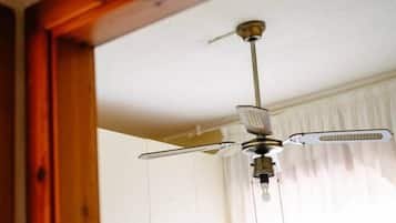 A room with a ceiling fan, white curtains, and a bed.