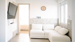 Un saló modern amb un sofà seccional blanc, un televisor de pantalla plana penjat a la paret i un rellotge de fusta.
