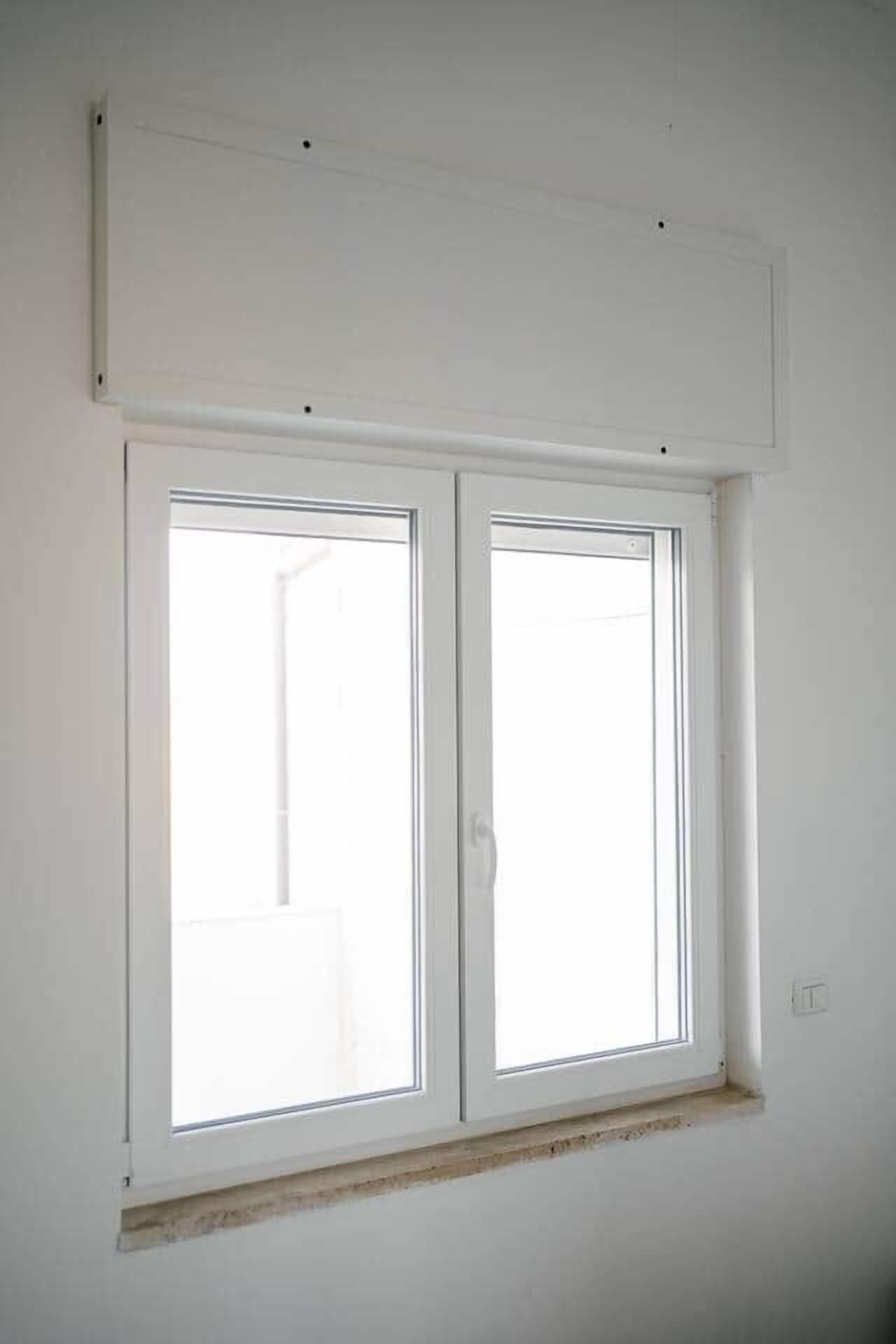 A room with a large window, a white wall, and a visible electrical outlet.