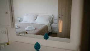 Habitació d'hotel amb llit, taula de nit i mirall que reflecteix l'espai.