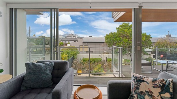 Ein modernes Wohnzimmer mit einem großen Schiebeglasfenster, das auf einen Balkon mit Blick auf die Umgebung führt.