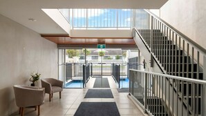 Eine Hotelhalle mit Treppe, einer Rezeption und Blick ins Freie.