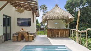 Un espace piscine doté d’un bar et de sièges, une structure à toit de chaume et un téléviseur fixé au mur.