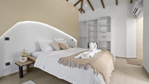 Une chambre moderne avec une tête de lit incurvée, un grand lit avec du linge de lit blanc, une table de chevet ornée d’un vase et une armoire intégrée.
