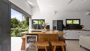 Une cuisine moderne dotée d’un îlot central, de meubles blancs et d’une grande fenêtre donnant sur un espace verdoyant.