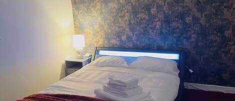 A neatly made bed with white linens and a red blanket, a bedside lamp, and a wall with a textured pattern.
