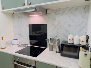 A modern kitchen with a black induction cooktop, a microwave, and a built-in oven. There are utensils in a holder and a toaster on the counter. - Elegant Escape in North Shields - Spacious 3 Bedroom House (North Shields)