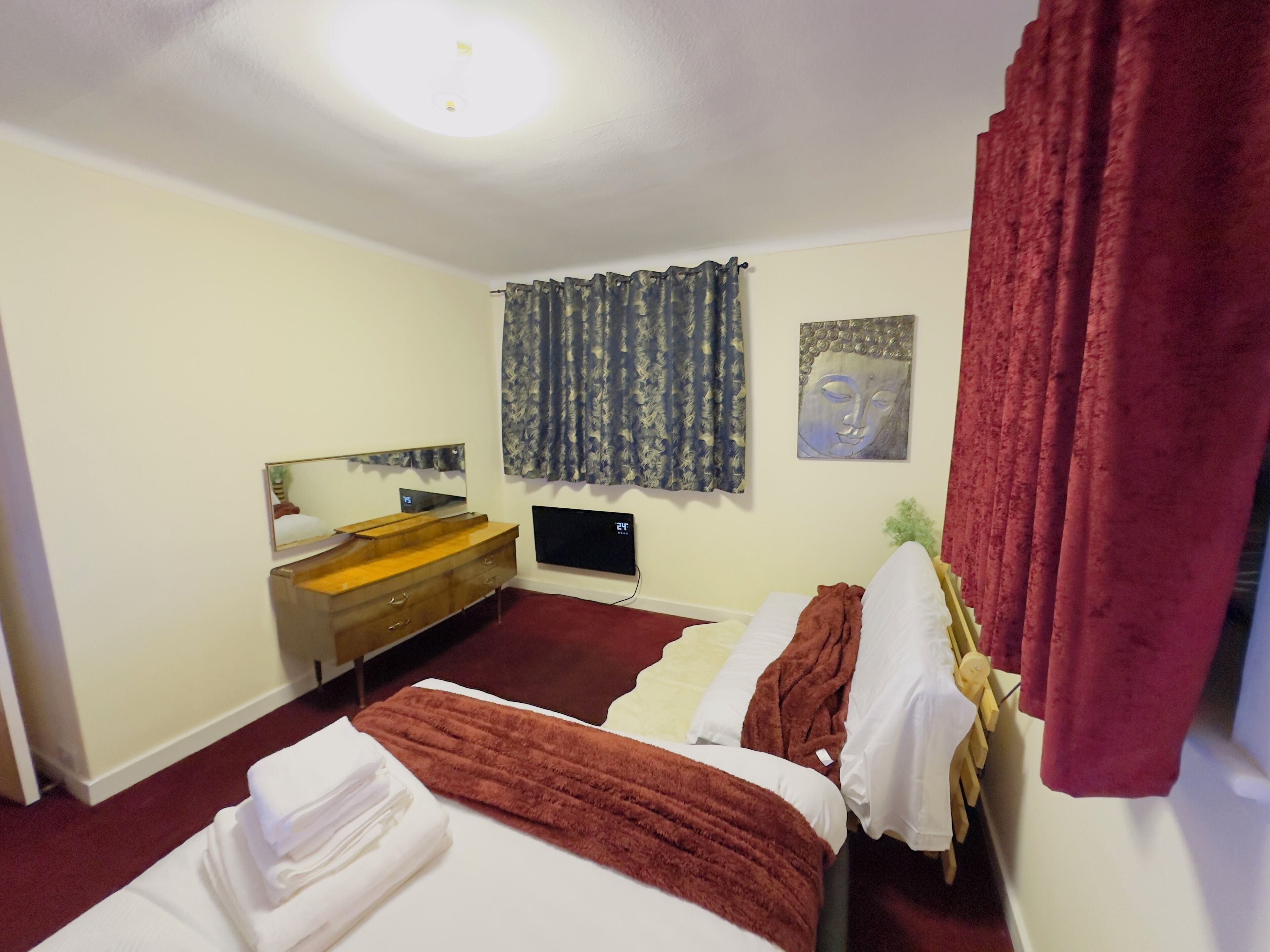 A hotel room with a bed, a wooden dresser, a flat-screen TV, and a Buddha painting on the wall.