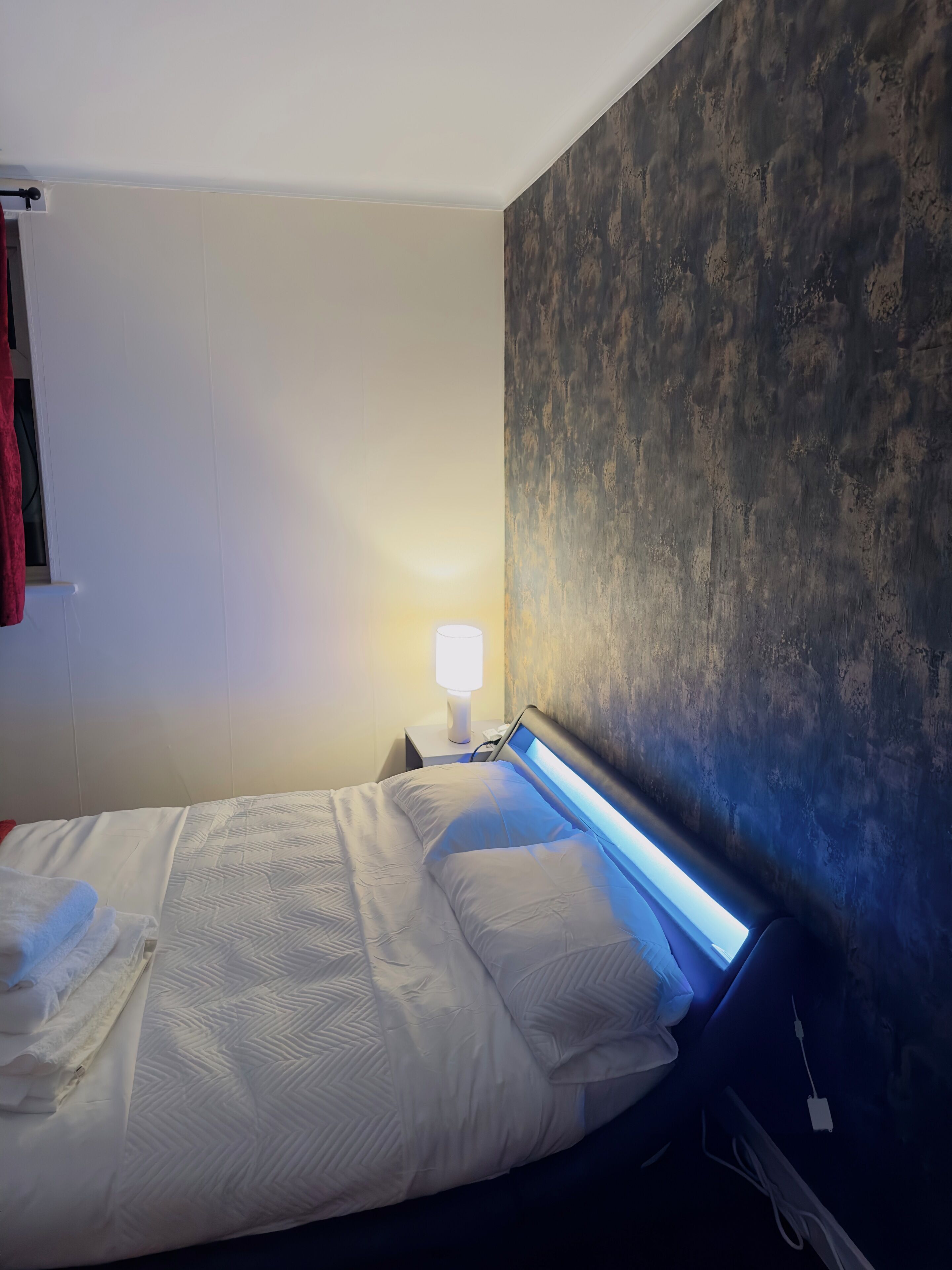 A hotel room with a bed, a nightstand with a lamp, and a textured wall.