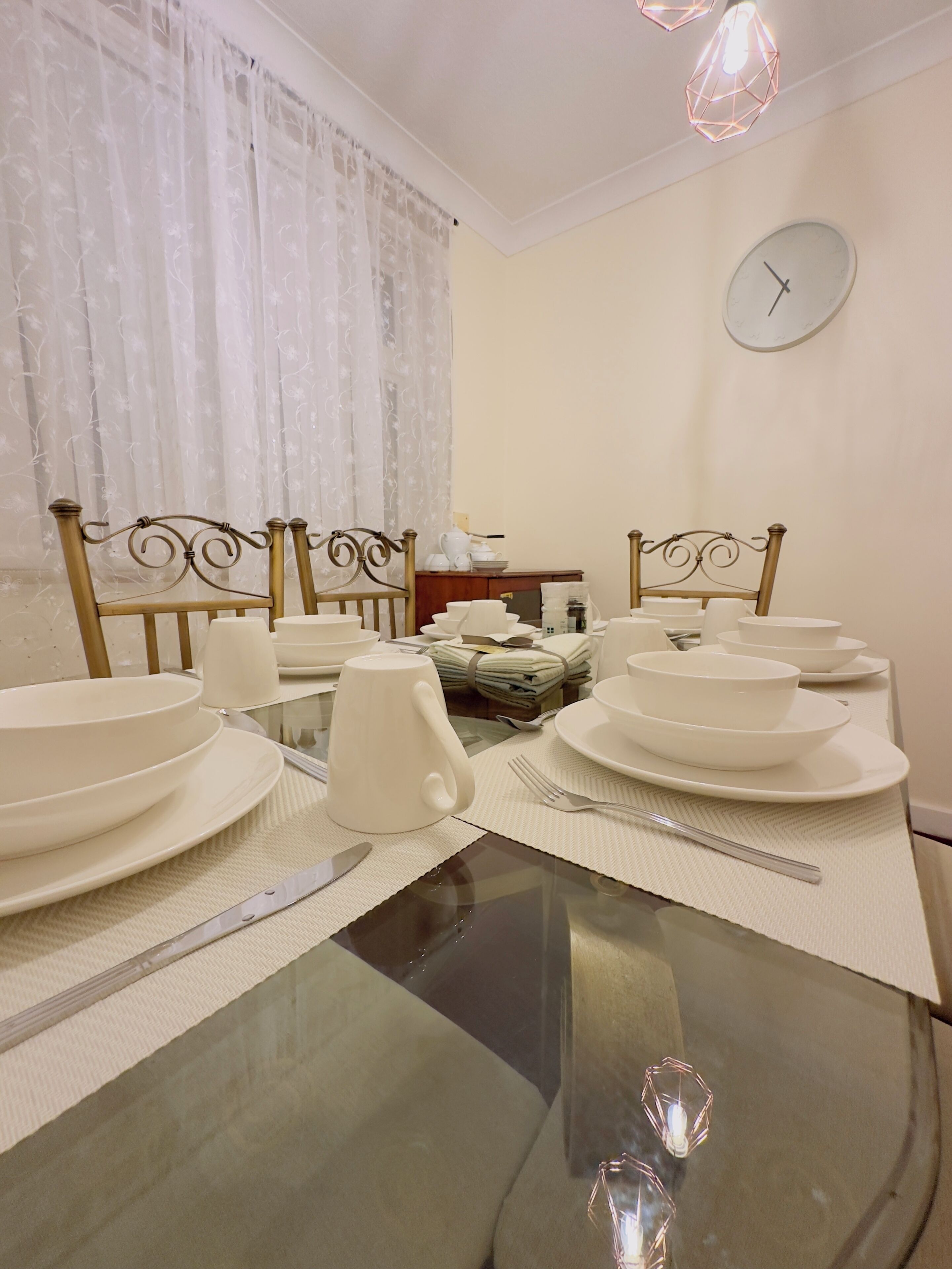 A dining table set with white plates, bowls, and a teapot, surrounded by chairs with ornate metal frames.