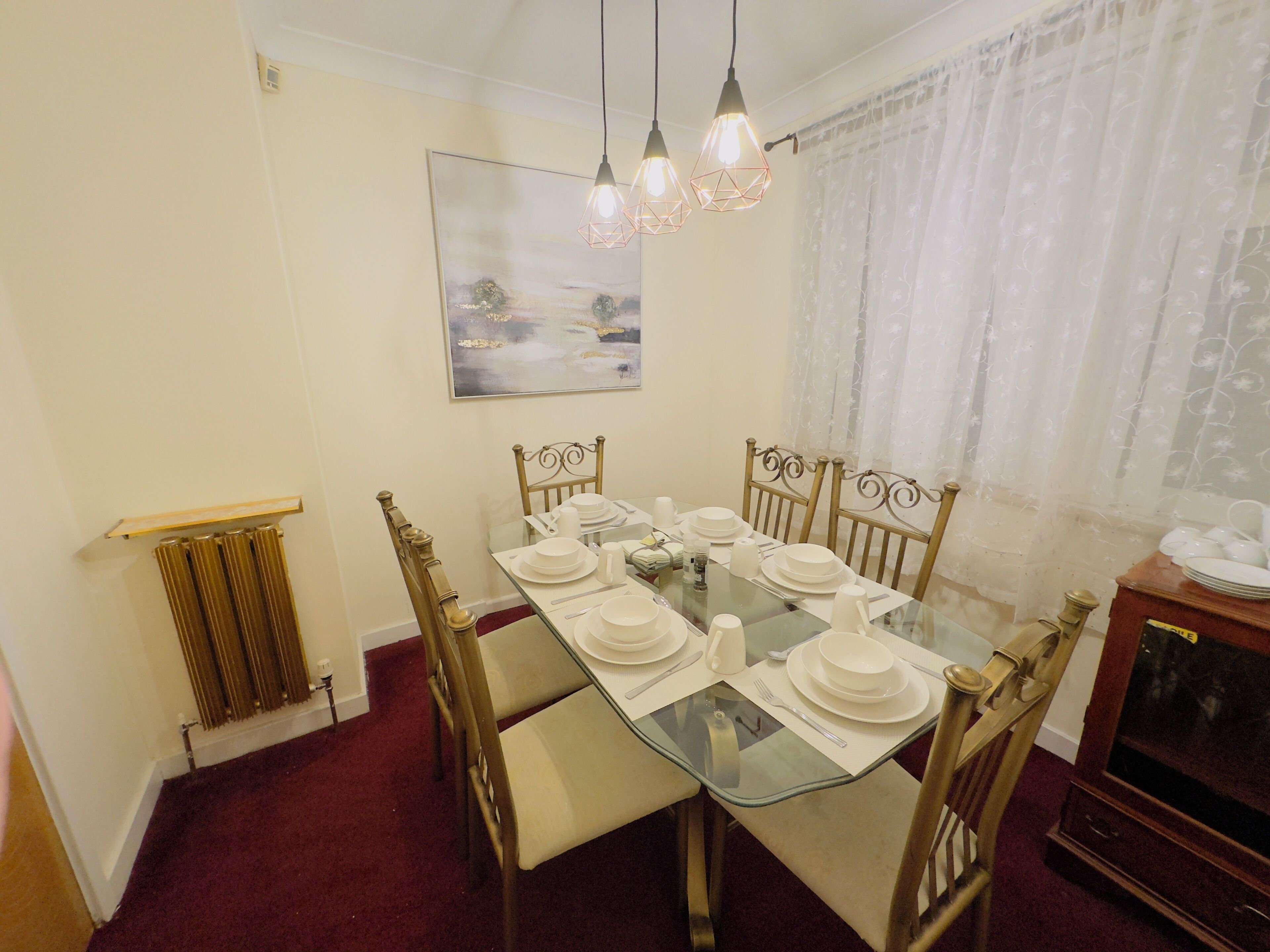 A dining room with a glass table set for six, surrounded by wooden chairs.