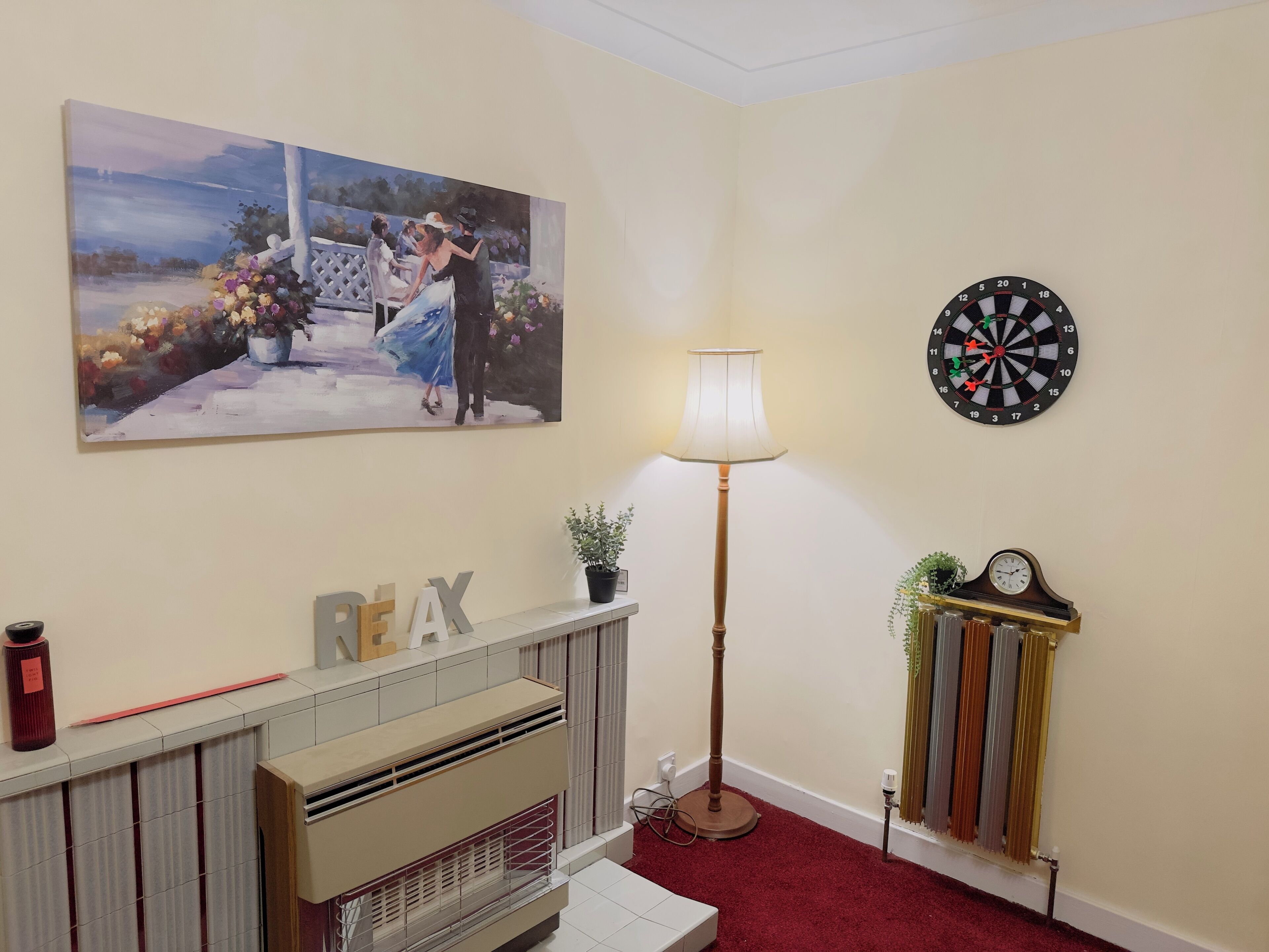 A room with a fireplace, a painting, a dartboard, and a radiator.