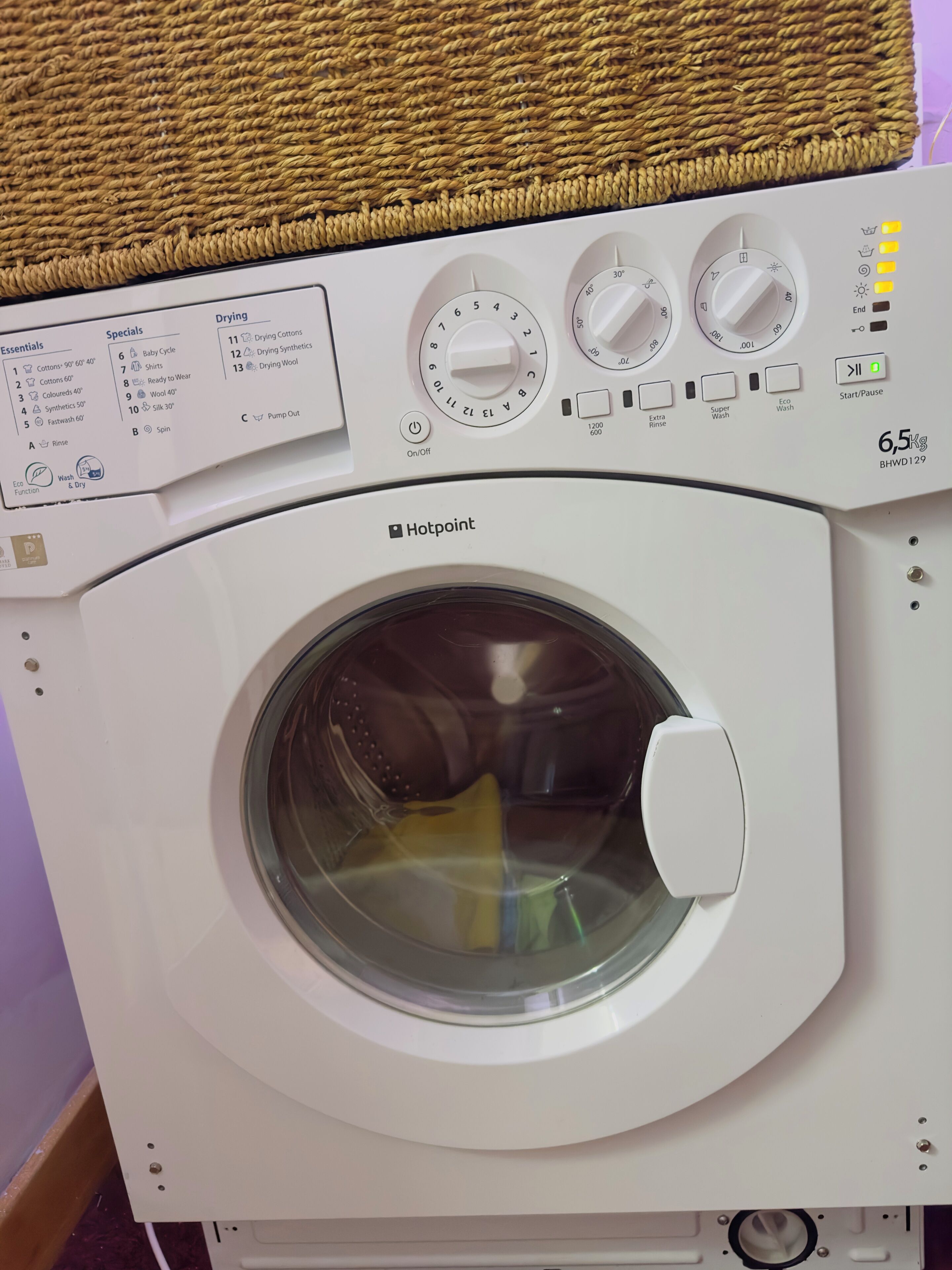 En bild som visar en Hotpoint-tvättmaskin framifrån, med vred för inställningar, en etikett med tvättråd och en indikator som visar tvättmaskinens kapacitet på 6,5 kg.
