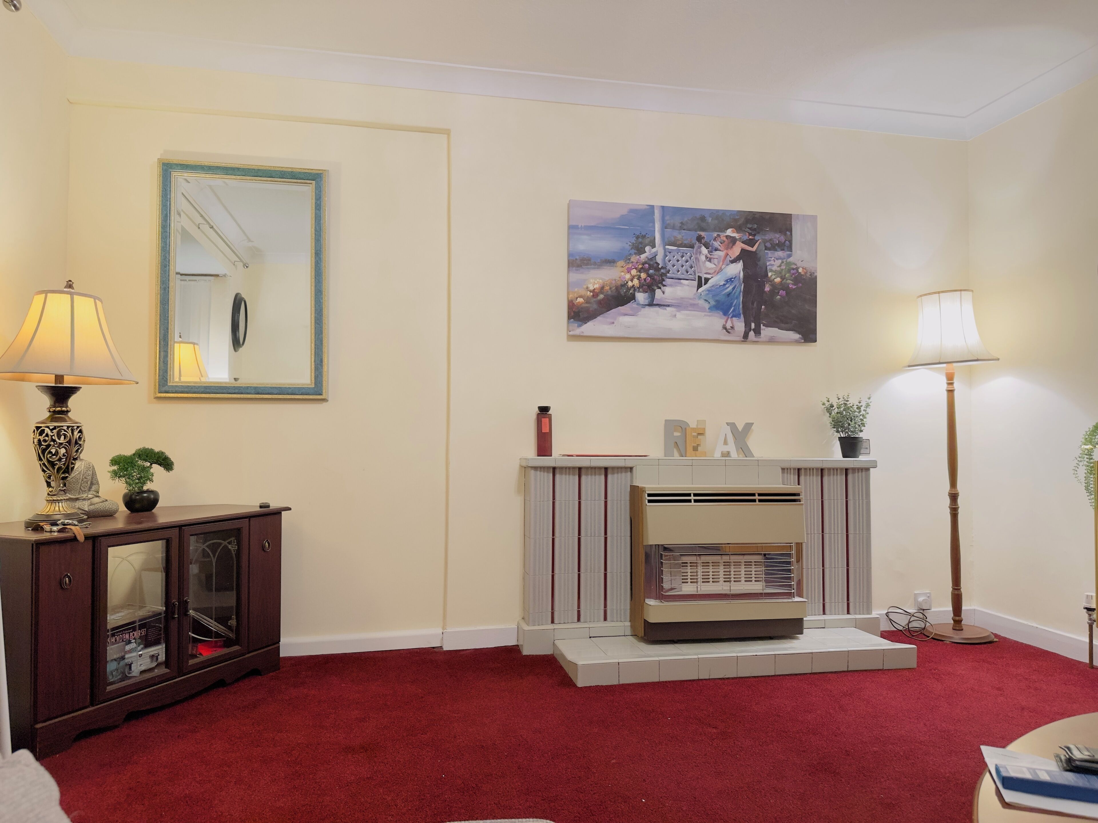 A living room with a fireplace, a cabinet with glass doors, a red carpet, and a painting on the wall.