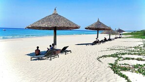 Een strand met rieten parasols en ligbedden.
