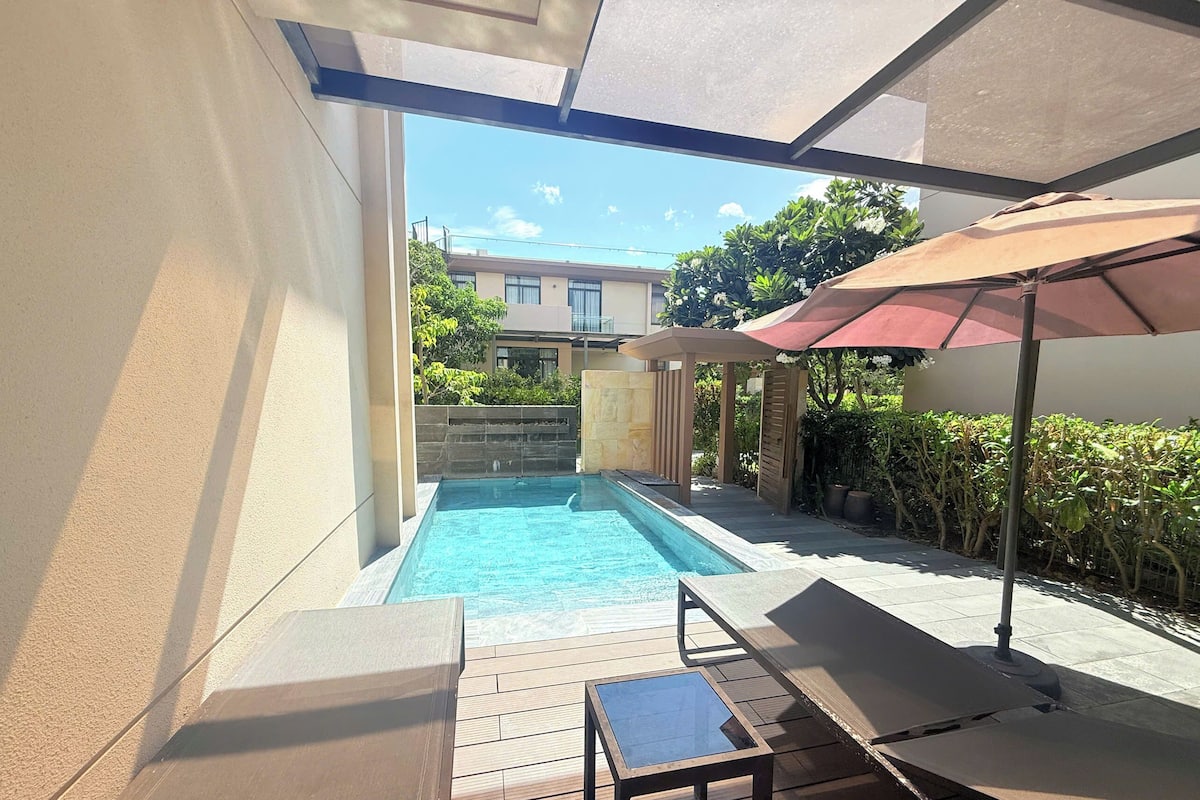 Una piscina con cubierta de madera, una mesa y una sombrilla.