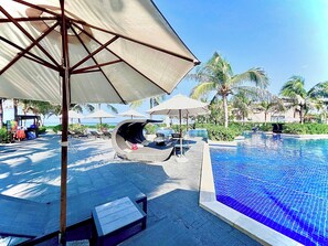 A pool area with lounge chairs and umbrellas, surrounded by palm trees and a clear sky. - Deluxe Villa Beach Front (Cam Lam)