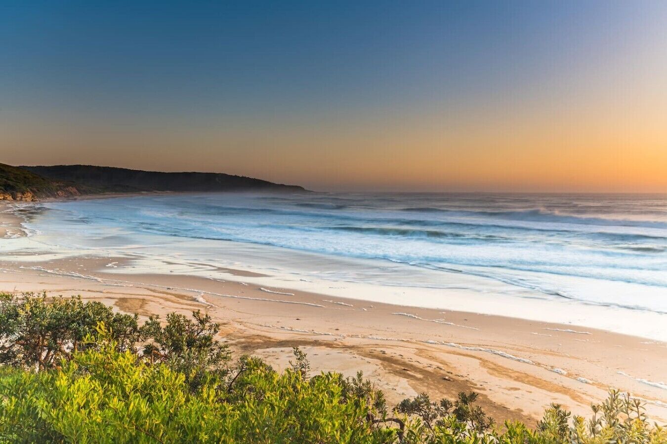 A beach with waves, greenery, and a clear sky.