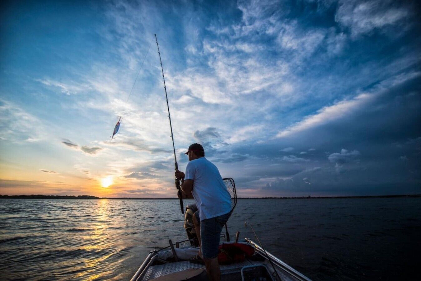 A person fishing on a boat with a sunset in the background.