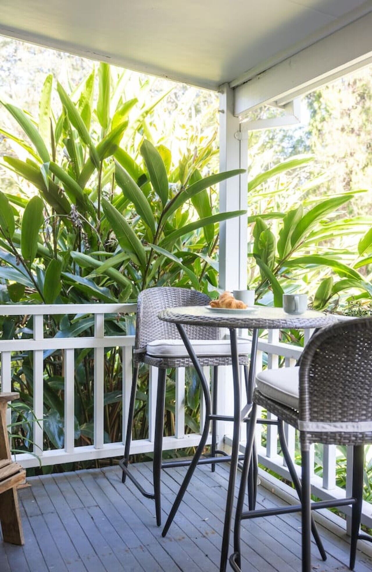 A covered outdoor area with a table and chairs, surrounded by lush green plants.