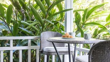 A covered outdoor area with a table and chairs, surrounded by lush green plants.