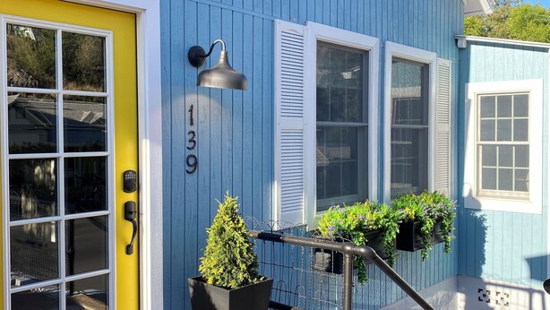 Une maison bleue avec une porte jaune, une boîte aux lettres noire et un parapluie rouge.