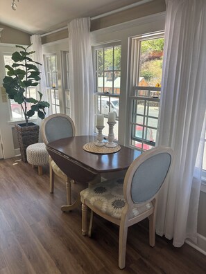 Un coin repas avec une table en bois, deux chaises, une plante en pot et une vue dégagée grâce à de grandes fenêtres.