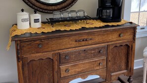 Une commode en bois avec un miroir, une machine à café et des bocaux étiquetés « Café » et « Sucre ».
