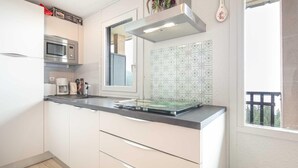 A modern kitchen with white cabinets, a stainless steel microwave, a glass-top island, and a window with a view of greenery. - Valley-view Apartment in Chamrousse (Chamrousse)