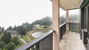 A balcony with a view of a lake, buildings, and forested hills. - Valley-view Apartment in Chamrousse (Chamrousse)