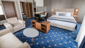 Une chambre d’hôtel avec un grand lit, un canapé, un téléviseur posé sur un meuble en bois et une petite table ronde.