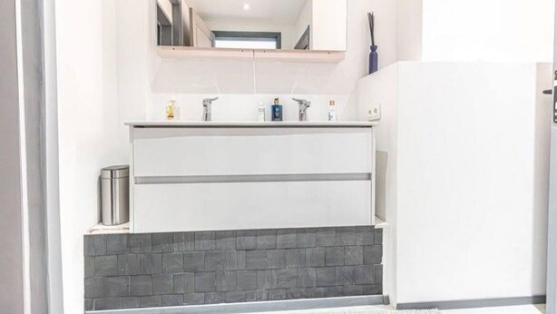A modern bathroom with a white vanity, a large mirror, and a gray tiled backsplash.