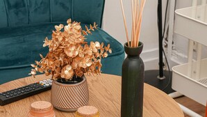A round wooden table with a potted plant, two jars, and a vase with reed sticks.