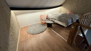 A loft bedroom with a sloped ceiling, a bed, a small table, and a chair.