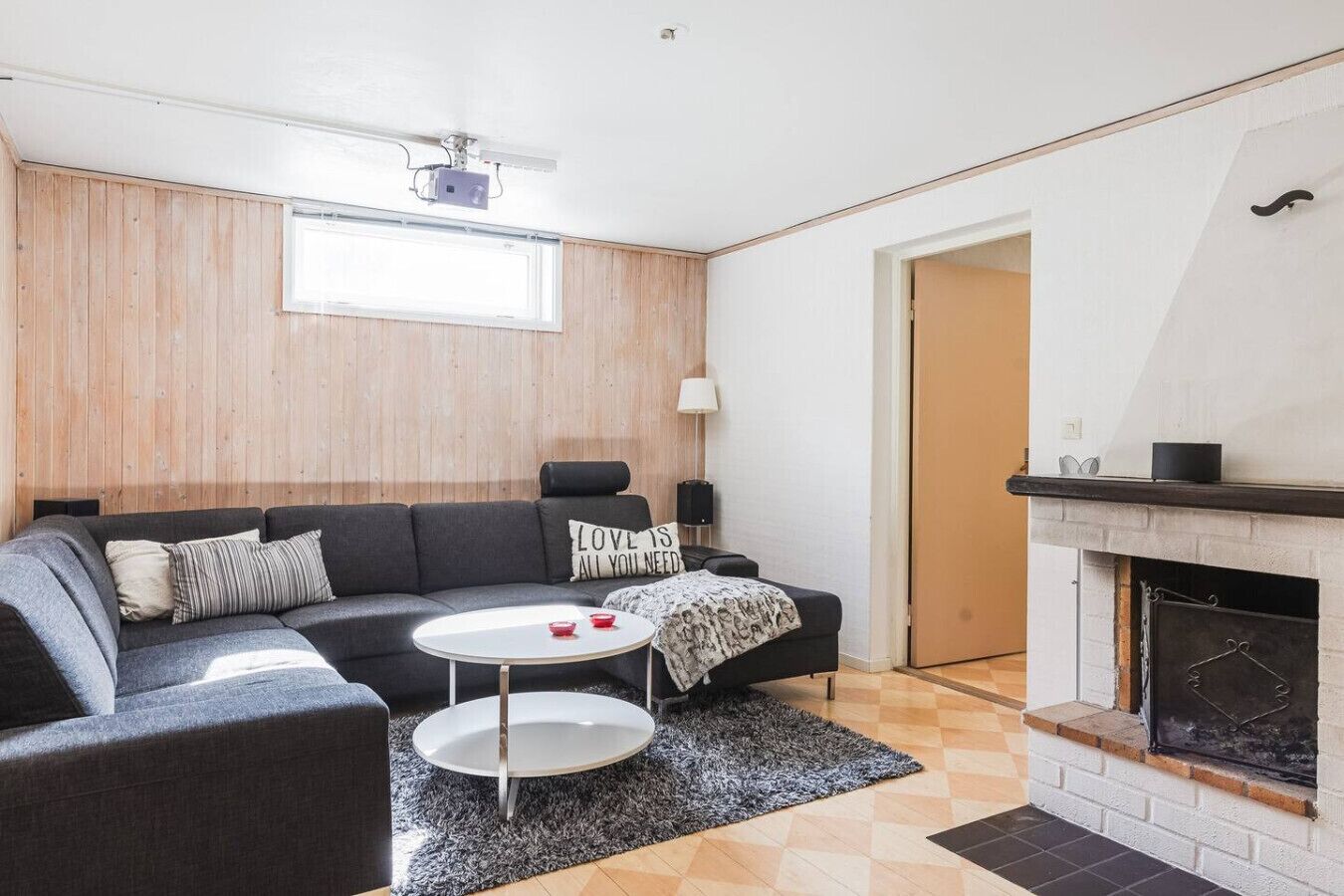 A modern living room with a sofa, a small round table, a fireplace, and a wooden wall panel.