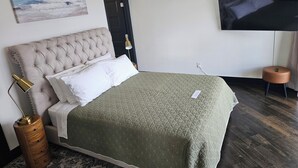 A neatly arranged bedroom with a large bed, a bedside lamp, a wooden nightstand, and a flat-screen TV mounted on the wall. - Industrial modern house with Water Views – Walk to the waterfront (Tacoma)