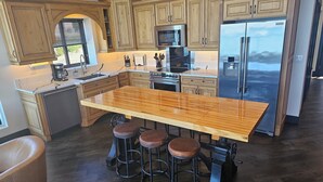 A kitchen with wooden cabinets, a stainless steel refrigerator, a microwave, and a large island with stools. - Industrial modern house with Water Views – Walk to the waterfront (Tacoma)