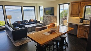 A modern kitchen with a wooden table and bar stools, a sofa, and a large window overlooking a body of water. - Industrial modern house with Water Views – Walk to the waterfront (Tacoma)