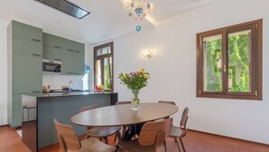 Una cocina moderna con gabinetes verdes, una mesa de comedor redonda con sillas de madera, un florero con flores y una ventana con vista a vegetación.