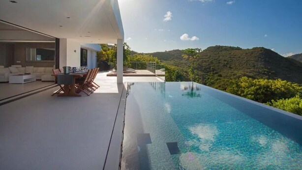 A modern outdoor pool area with a dining setup and a view of the surrounding hills.