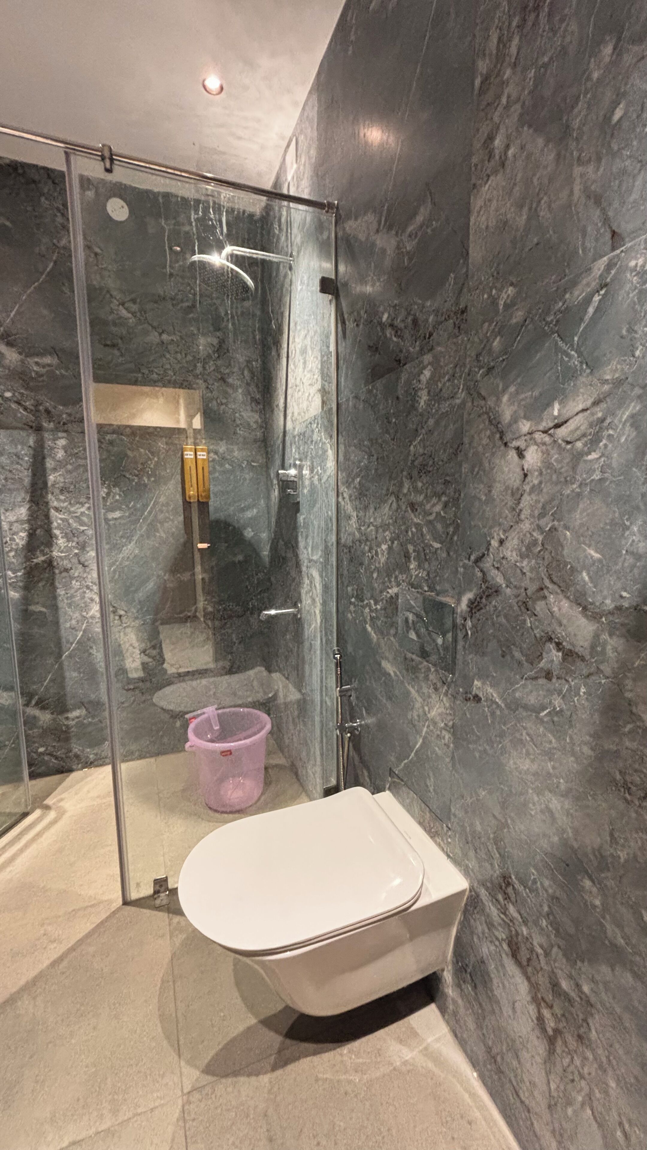 Une salle de bain moderne avec une douche en verre, des toilettes blanches et des murs en marbre.