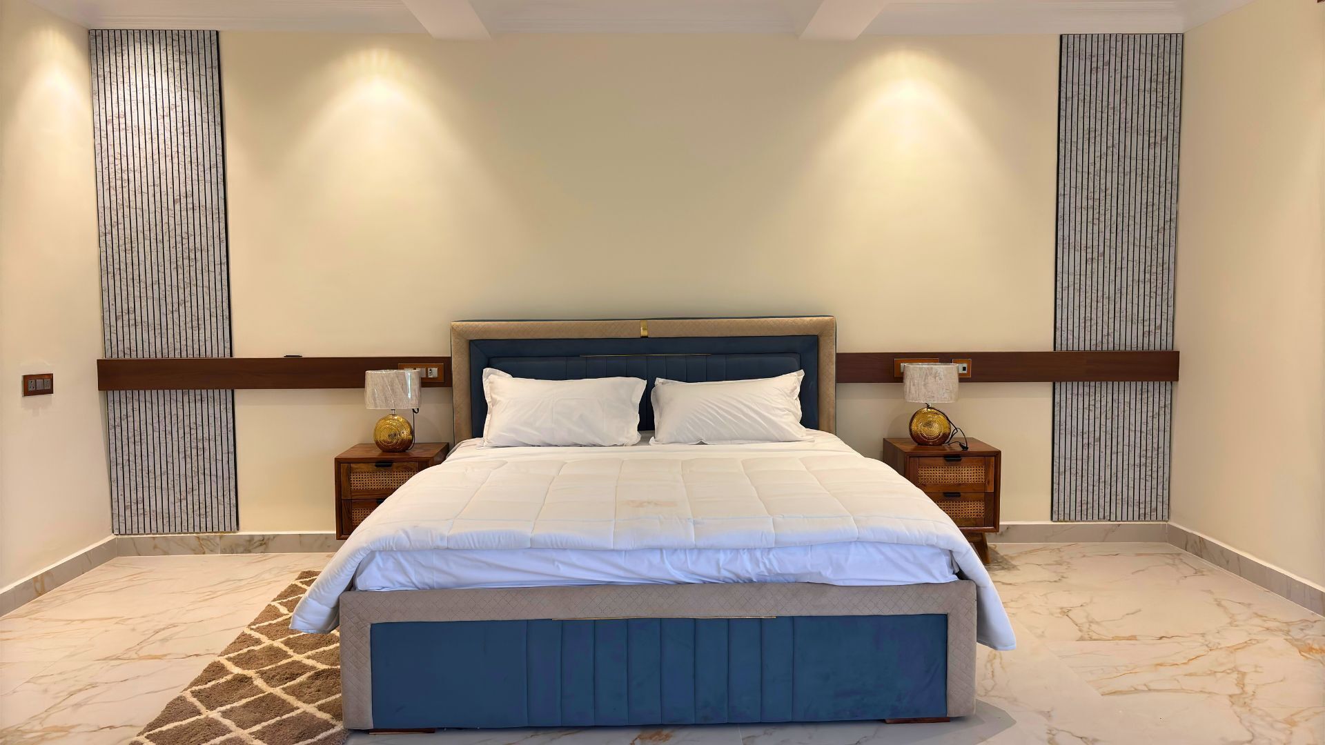 A neatly arranged bedroom with a large bed, two bedside tables with lamps, and a marble-patterned floor.