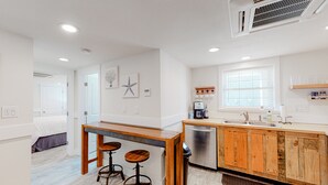 A modern kitchen with wooden cabinets, a built-in dishwasher, and a bar area with stools. - KH3111B: Seas the Day | Walk to Beach | Patio | Kitchenette (Kitty Hawk)
