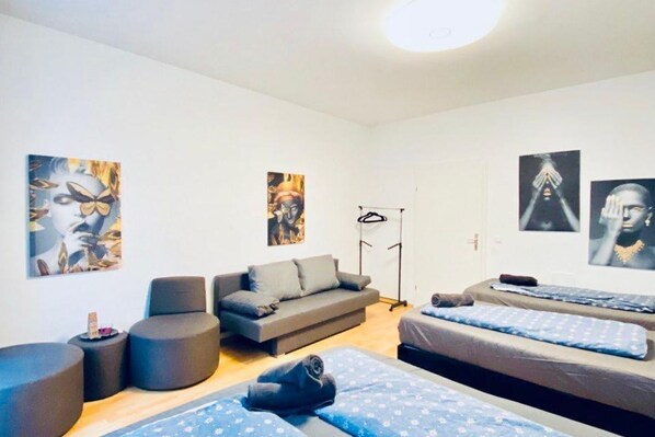 Une pièce comprenant un canapé, deux fauteuils, un lit avec une couvre-lit à motifs et des œuvres d’art accrochées aux murs.